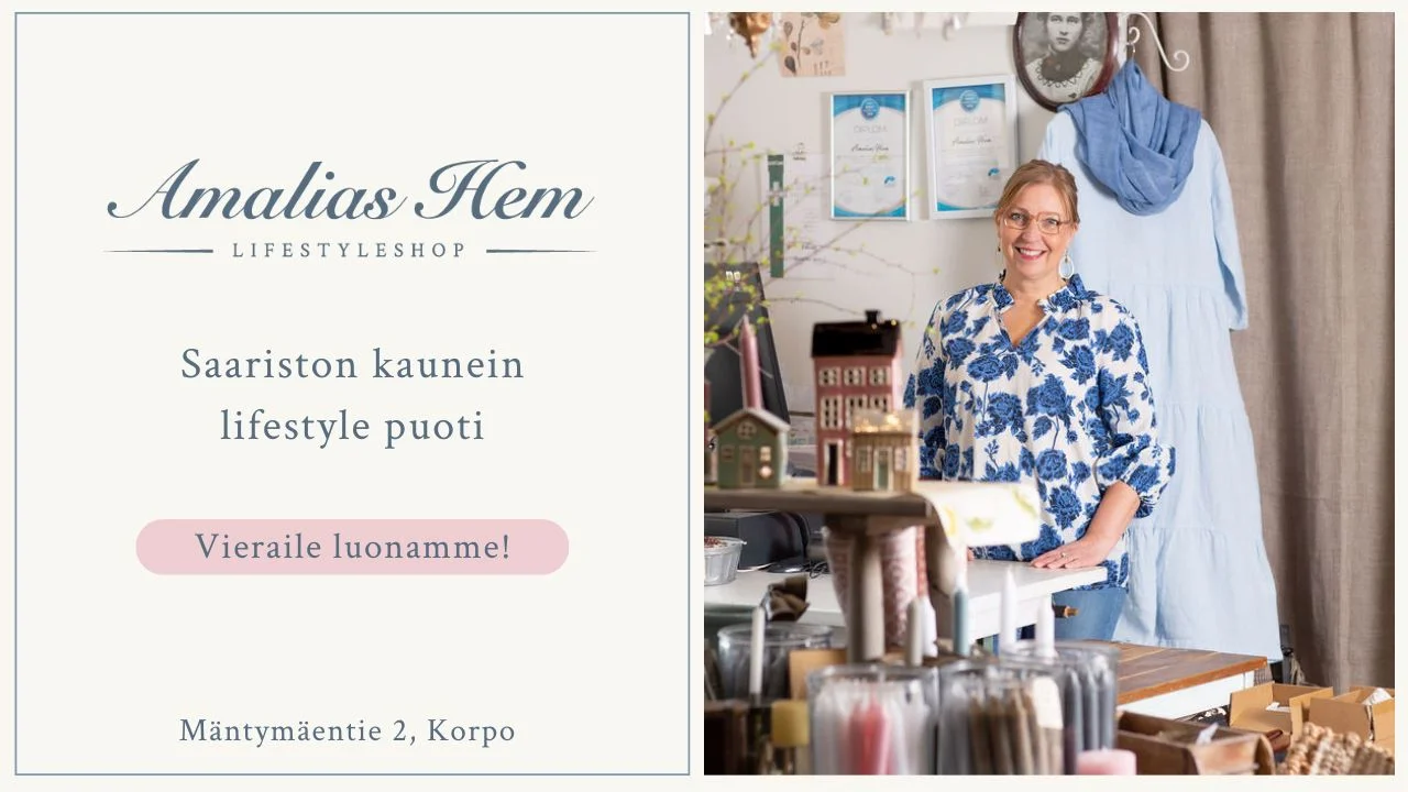 Kukkamekkoon pukeutunut nainen seisoo lifestyle-liikkeen tiskin takana. Myymälässä on erilaisia kodin sisustustarvikkeita. Tekstissä lukee "Amalia's Home Lifestyleshop, Särgårdenin kaunein lifestyle-myymälä, Käy meillä!