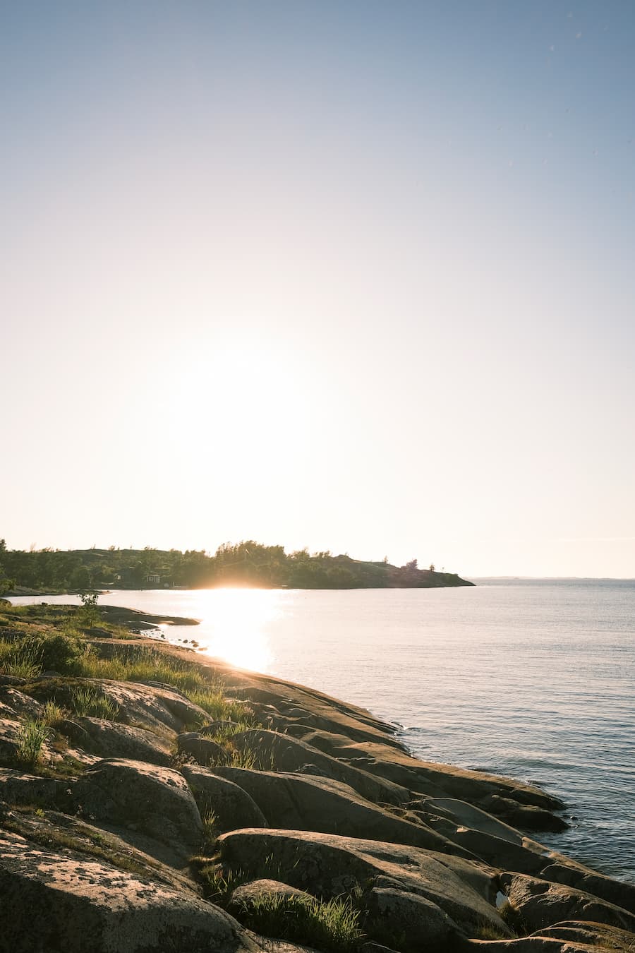 Auringonlasku kalliorannalla, jossa on rauhalliset vedet ja kirkas taivas.