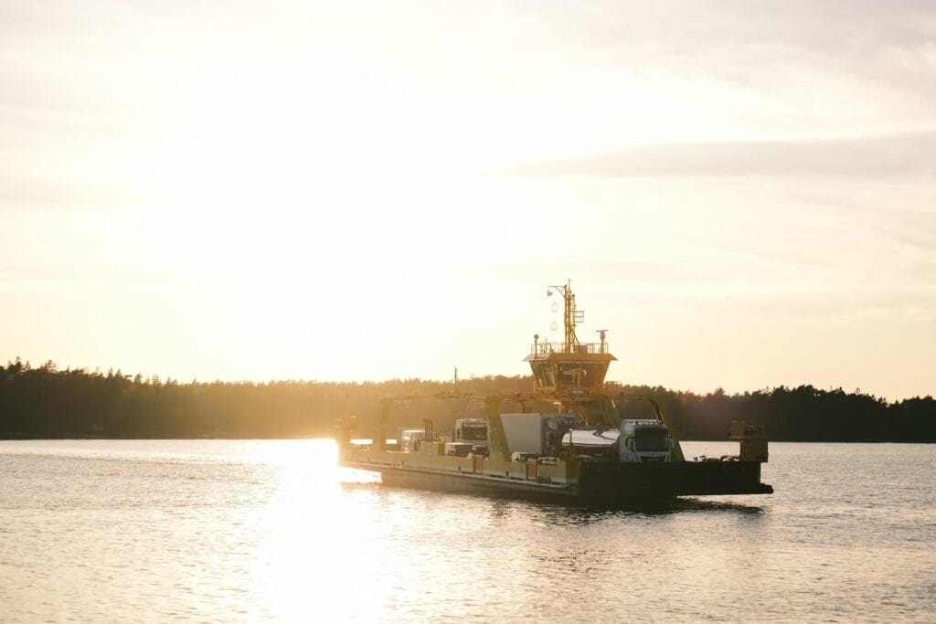 Ajoneuvoja kuljettava lautta ylittää rauhallisen vesistön auringonlaskun aikaan.