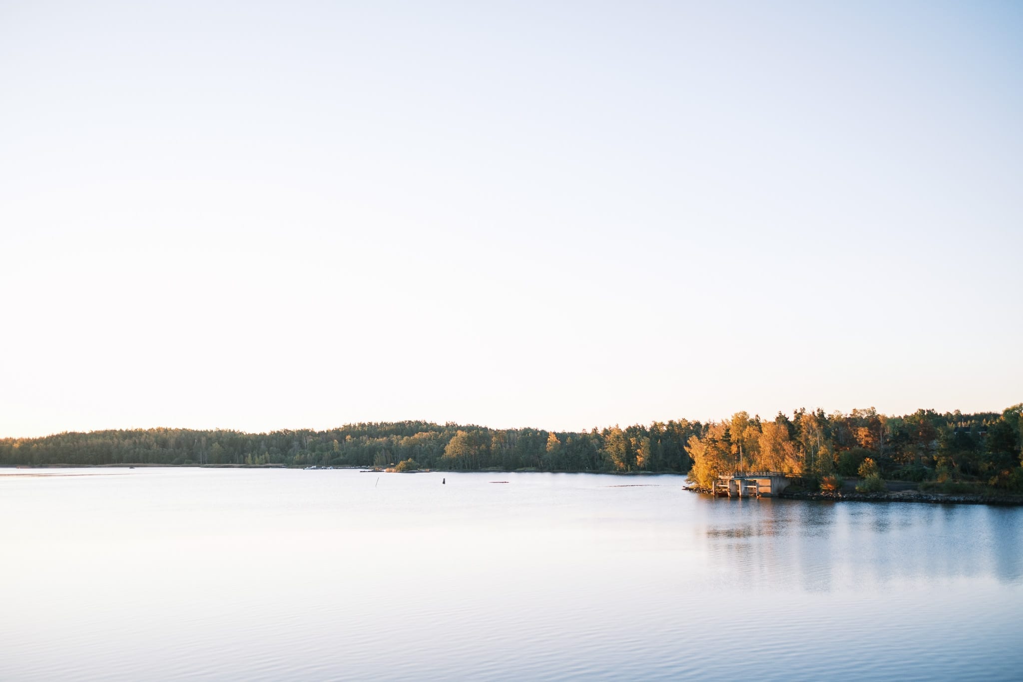 Rauhallinen järvi heijastaa kirkkaansinistä taivasta, ja oikealla on pieni metsäinen saari, jossa näkyy syksyn lehdet.